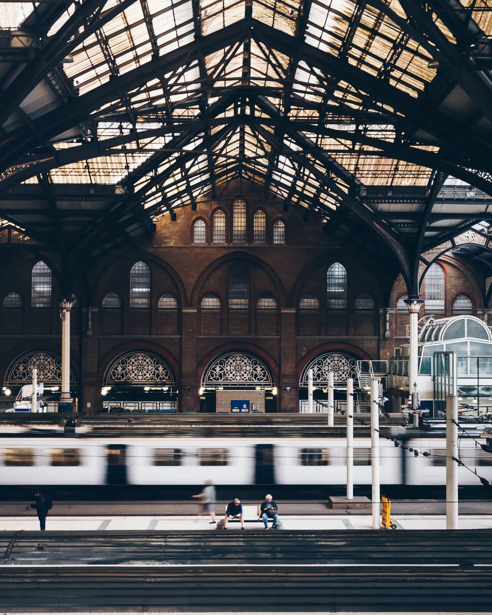 Liverpool Street station in London: the Victorian iron and glass roof over a train leaving the platform, with a few passengers waiting