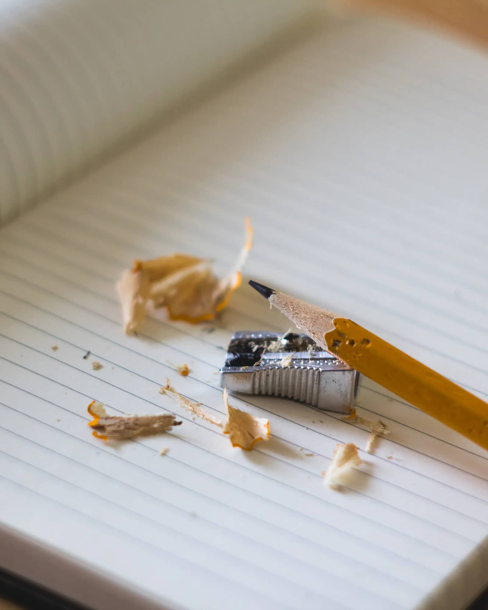 A freshly sharpened pencil, a sharpener and pencil shavings on a lined notebook
