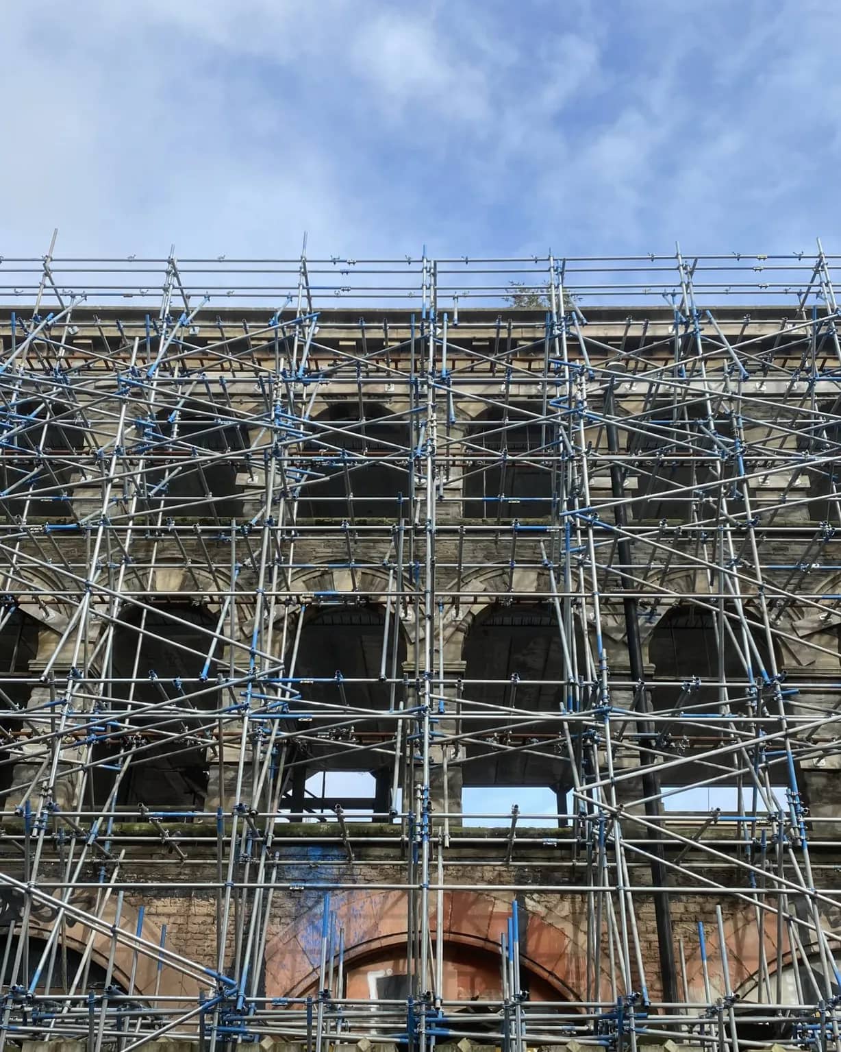 Scaffolding bracing the facade of an old brick and stone building, with sky showing through its empty windows